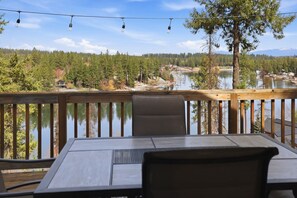 A wooden deck with a table and chairs overlooking a lake with boats, surrounded by trees and a clear sky. - Coeur d'Alene's Coeur de la Rivière (Coeur d'Alene)