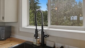 Eine Küche mit einem schwarzen Wasserhahn, einer Holzarbeitsplatte und einem Fenster mit Blick auf Bäume.