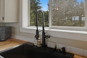 A kitchen with a black faucet, a wooden countertop, and a window with a view of trees.