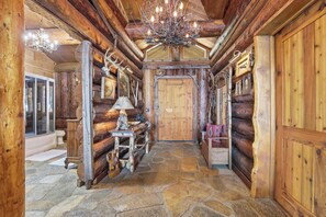 Ein Blockhaushaus-Interieur mit Steinboden, Holzwänden, einer Chandelüstere und einer Holztür.