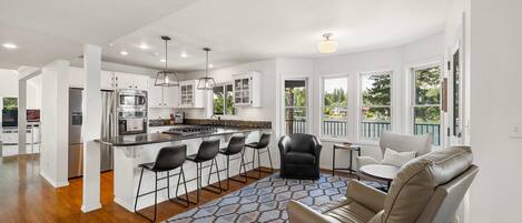 A modern kitchen with white cabinets, a central island, bar stools, and a dining area with a sofa and chairs.