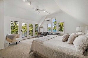A bedroom with a bed, a ceiling fan, a fireplace, and large windows.