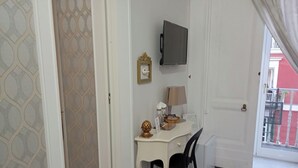 Ett rum med ett rutmönstrat golv, ett vitt skrivbord med en lampa, en stol och en tv som är monterad på väggen.