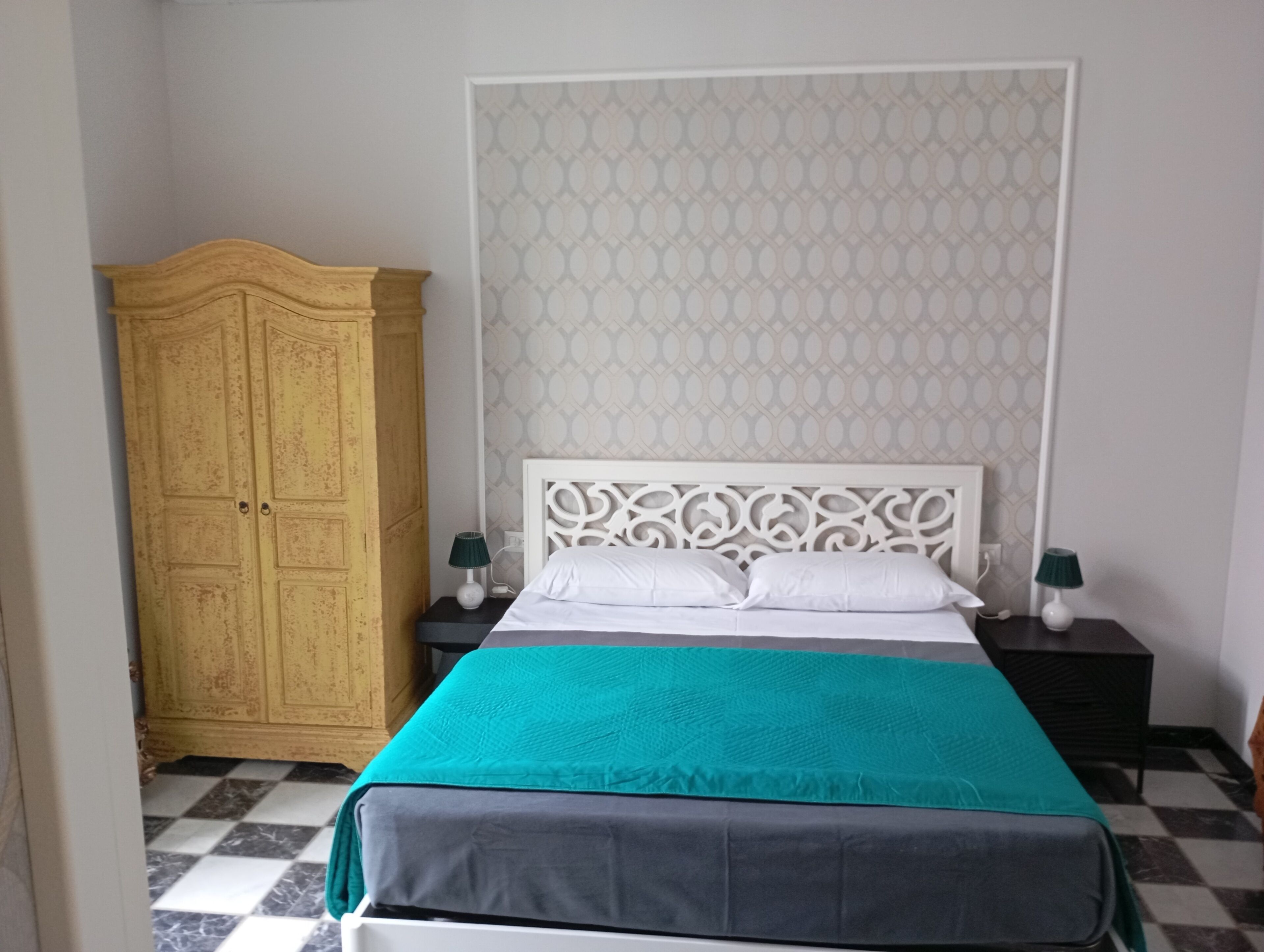 A bedroom with a bed, two bedside tables, a wardrobe, and patterned wallpaper.