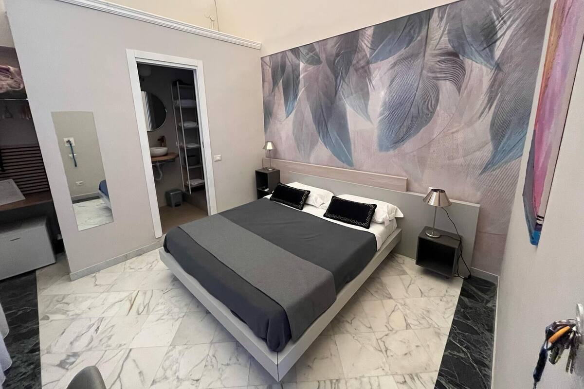 A modern bedroom with a large bed, a walk-in closet, a bathroom, and a large abstract painting on the wall.