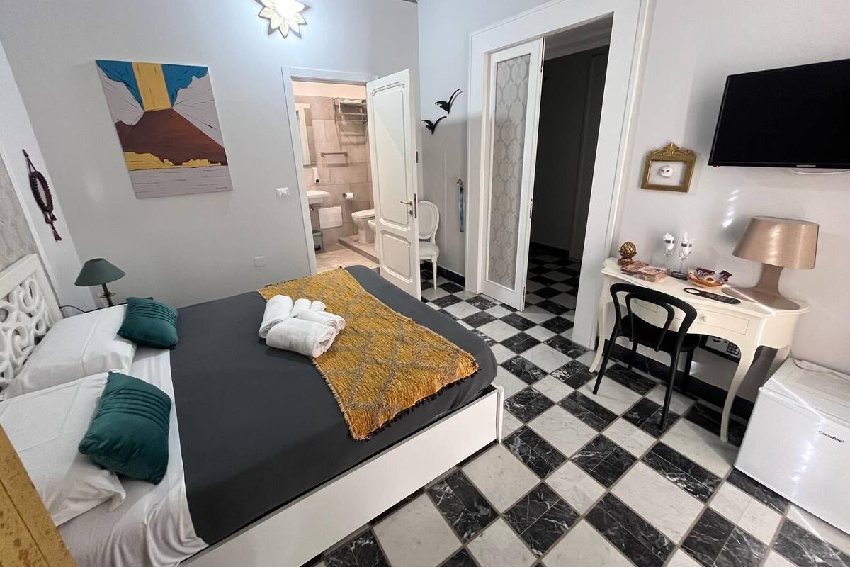 A hotel room with a bed, a desk, a chair, a television, and a bathroom visible through an open door.
