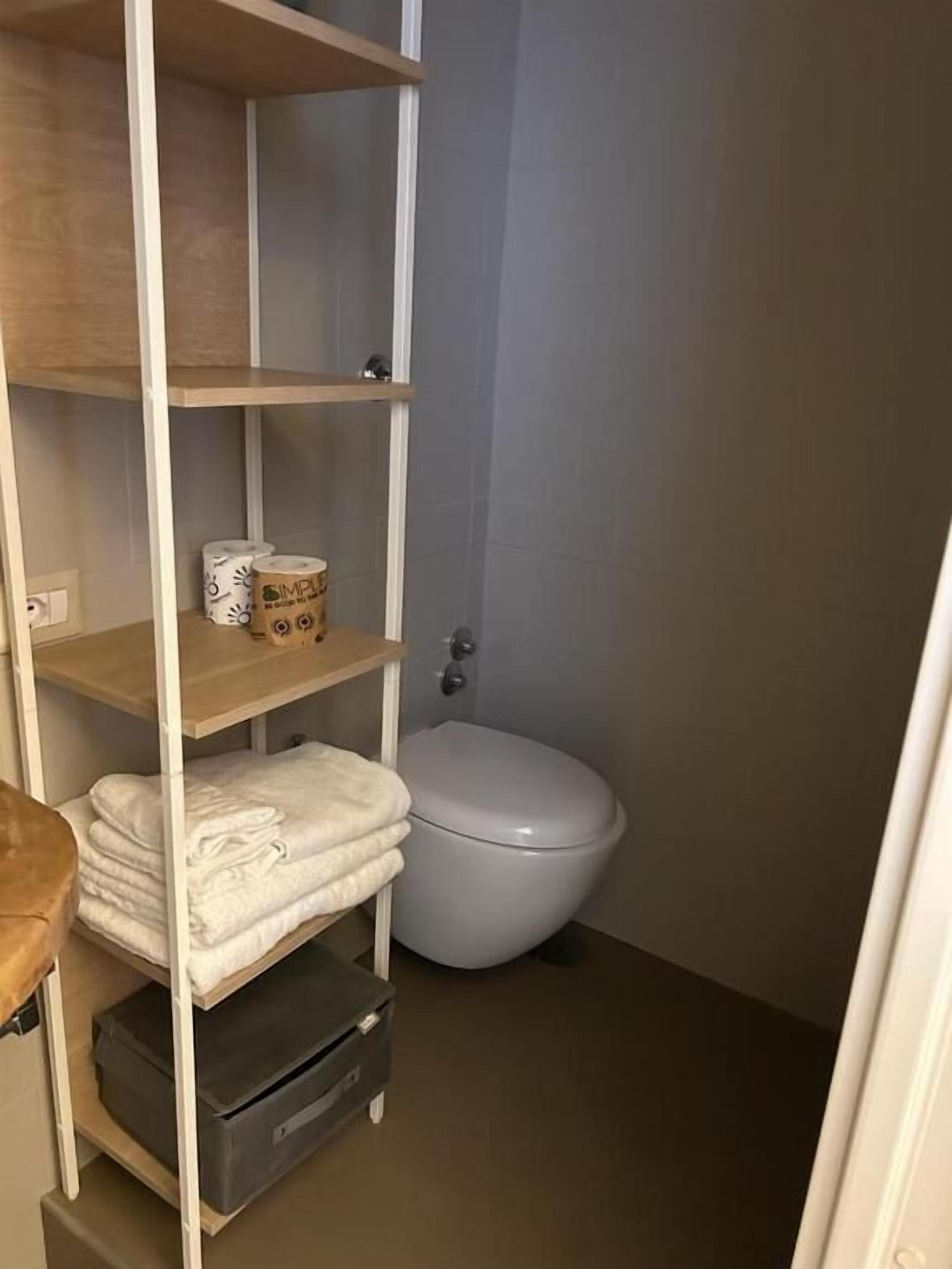 A small bathroom with a toilet, a shelf with towels, and a storage unit.