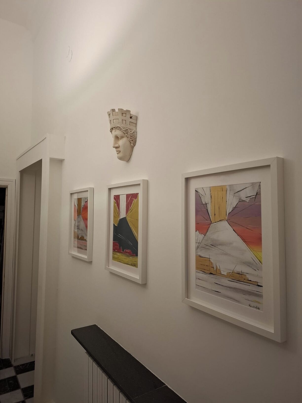 Een gang met ingelijste kunstwerken aan de muur en een decoratief element erboven.