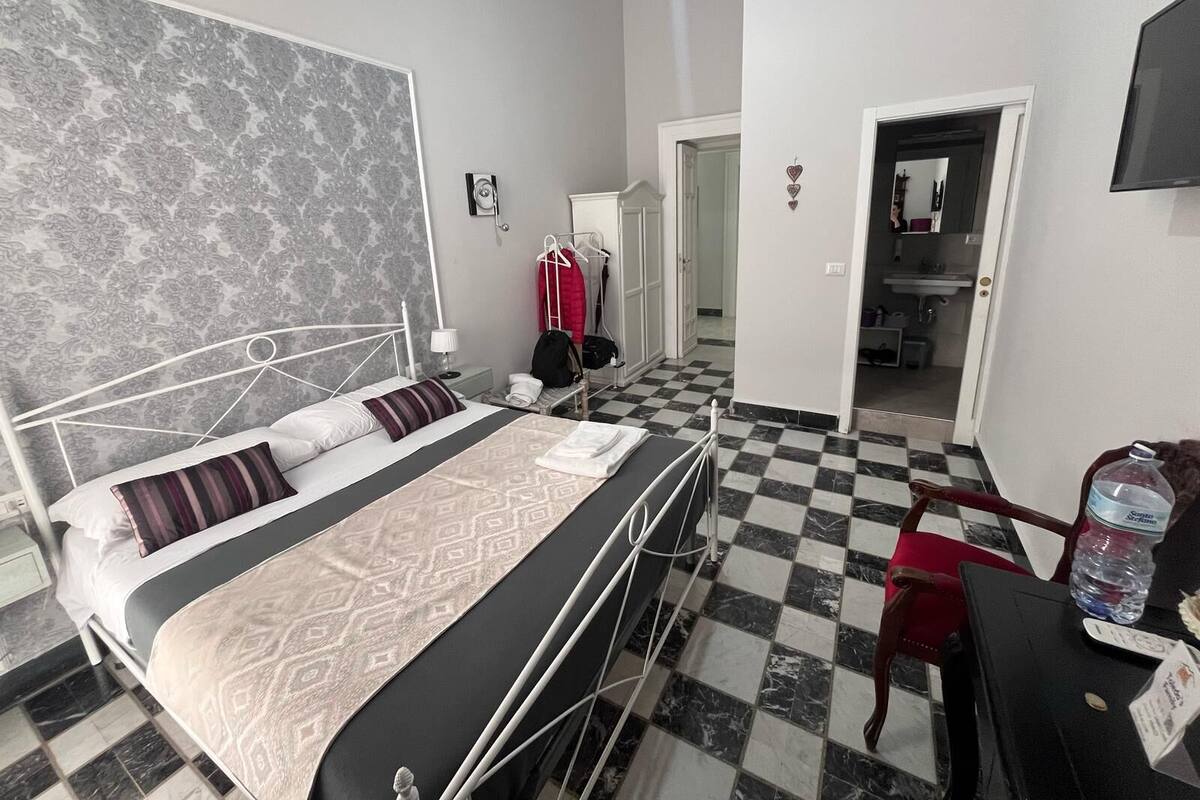 A hotel room with a bed, a desk, a chair, a wardrobe, and a bathroom visible through an open door.
