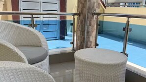 Wicker furniture with cushions, a glass balustrade, and a view of a pool. - Cozy house a few minutes from HOMS (Santiago de los Caballeros)