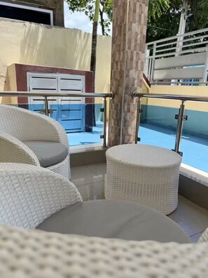 Korbmöbel mit Kissen, eine Glasreling und Blick auf einen Pool.