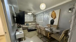 A modern living room with a flat-screen TV, a dining area with a glass table, and a sofa set. - Cozy house a few minutes from HOMS (Santiago de los Caballeros)