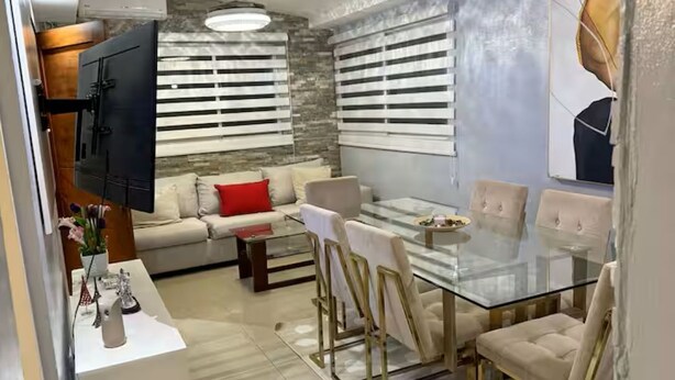 A modern living room with a glass dining table, white sofas, and a TV mounted on the wall. - Cozy house a few minutes from HOMS (Santiago de los Caballeros)