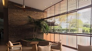 Un intérieur moderne avec un mur en pierre, une grande fenêtre avec des stores et un coin salon agrémenté d’une plante.