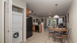 A compact kitchen with a washing machine, a refrigerator, and a dining area with a table and chairs. - Bluebonnet Poolside Paradise • Heated Pool • Schlitterbahn 5 Blocks • Sleeps 6 (New Braunfels)
