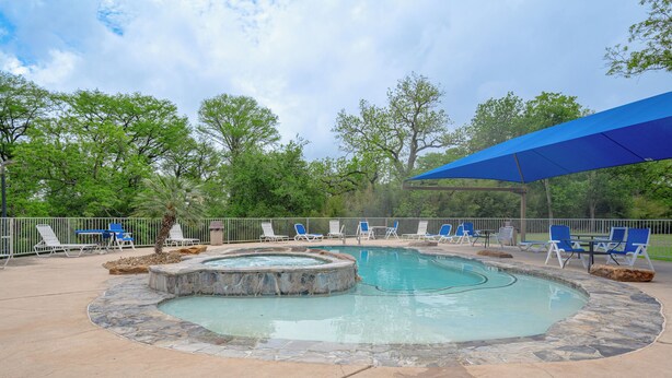 A swimming pool with a stone edge, surrounded by lounge chairs and a covered area. - Bluebonnet Poolside Paradise • Heated Pool • Schlitterbahn 5 Blocks • Sleeps 6 (New Braunfels)
