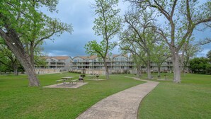 A grassy area with picnic tables and a concrete pathway leading to a building with multiple windows and balconies. - Bluebonnet Poolside Paradise • Heated Pool • Schlitterbahn 5 Blocks • Sleeps 6 (New Braunfels)