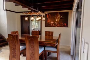 Un coin repas avec une table et des chaises en bois, un éclairage suspendu et un grand tableau accroché au mur.