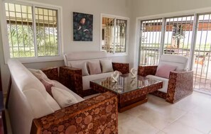 Un salon comprenant un canapé, des fauteuils, une table basse en verre et un tableau accroché au mur.