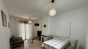 A dining area with a checkered tablecloth, a sofa, a TV, and a pendant light. - 2-bedr. apartment Palhinhas Historic Center 5 min. away (Albufeira)