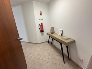 Ein Flur mit einem Feuerlöscher, einem Schild, einer Vase und einem Hinweisschild auf einem Tisch.