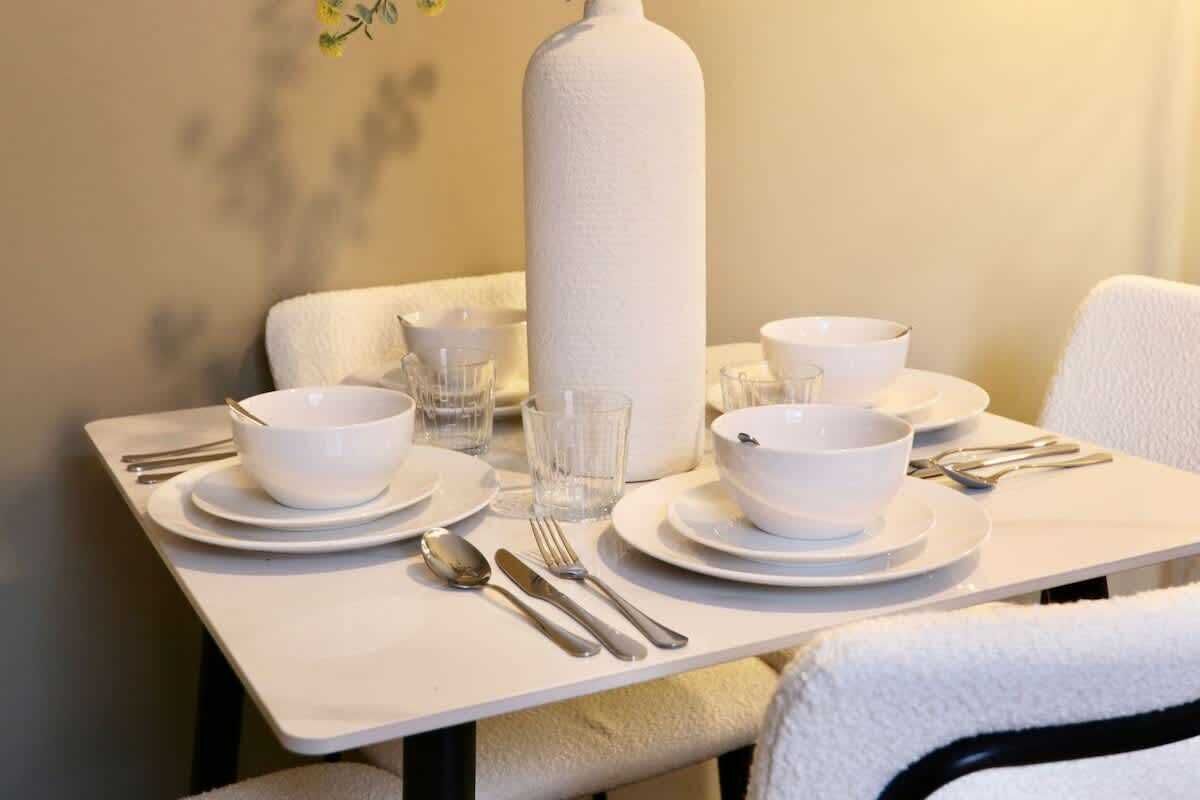 A neatly set dining table with white plates, bowls, glasses, and cutlery.
