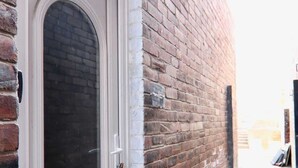 Eine weiße Tür mit kleinem Fenster, eine Ziegelwand und ein schmaler Betonweg.