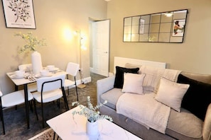 A living room with a sofa, a coffee table, a dining table with chairs, and a wall-mounted mirror. - Spacious 2BR Haven Near Sheffield Centre (Sheffield)