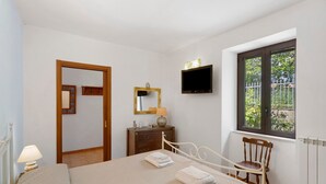 Une chambre à coucher avec un lit, une chaise, une commode, un téléviseur, une fenêtre et une porte.