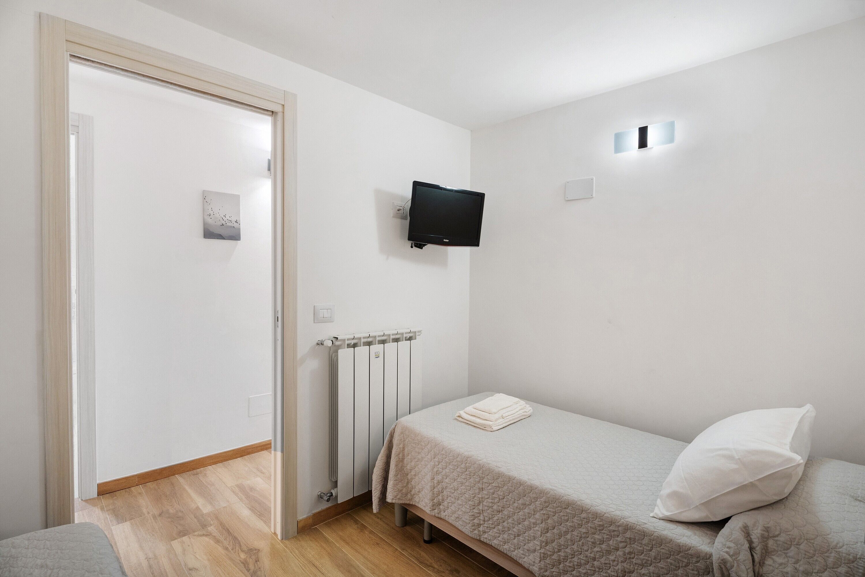 Ein kleiner, sauberer Raum mit einem Bett, einem an der Wand befestigten Fernseher und einer Heizung.