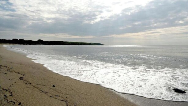 Ein Strand mit sandigem Ufer, Wellen und einem bewölkten Himmel.