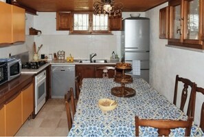 A compact kitchen with a dining table, wooden cabinets, a refrigerator, and a microwave.