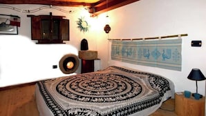 Ein Schlafzimmer mit einem gemusterten Bettüberwurf, einer Wandteppich, einem Holzkopfteil und einem kleinen Nachttisch mit Lampe.
