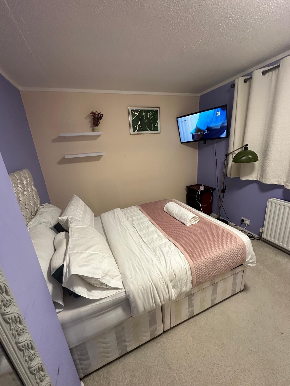 Una camera da letto con un letto, una televisione, una lampada e una mensola a parete.