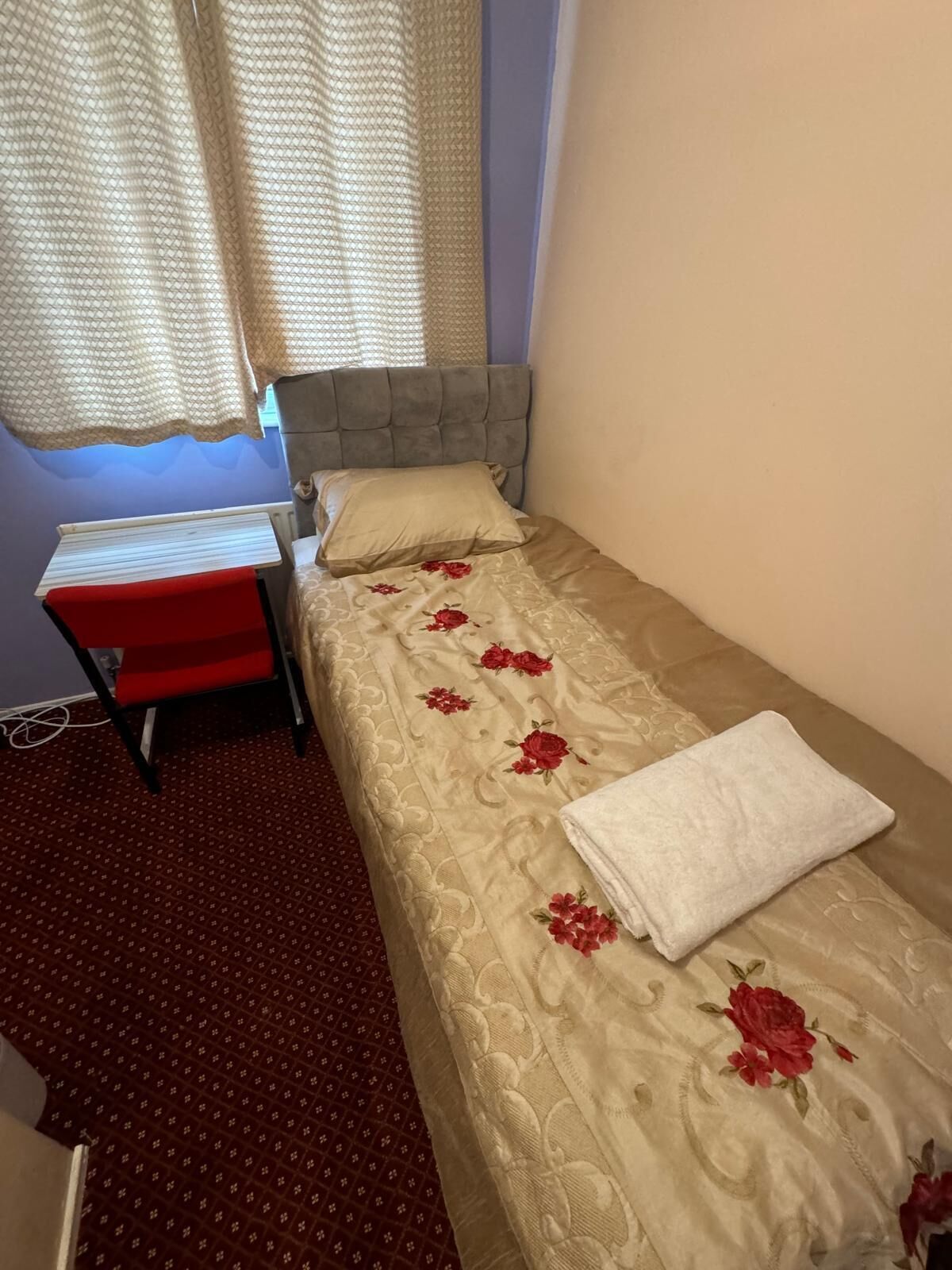 Una cama individual con una colcha estampada, una almohada blanca y una silla roja con cojín rojo.