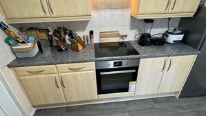 Una cocina con armarios de madera clara, una campana extractora de acero inoxidable, un horno empotrado y una encimera con diversas herramientas y electrodomésticos de cocina.
