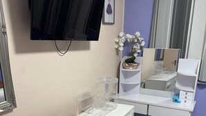 Un baño moderno con un tocador blanco, un televisor montado, un espejo y una orquídea en maceta.