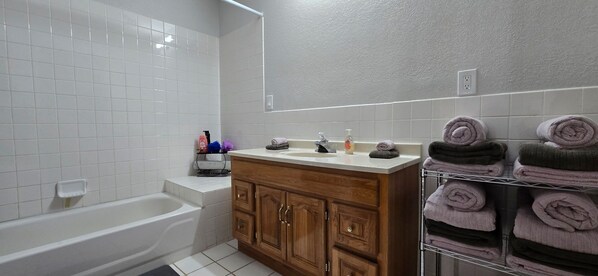 A bathroom with a white bathtub, a wooden vanity with a sink, and a towel rack with folded towels.