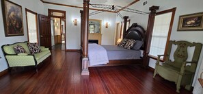 Una habitación con una cama con dosel, un sofá verde, una silla de madera y un espejo en la pared.