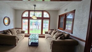 A living room with two sofas, a glass coffee table, and large windows with a view of a backyard. - Welcome to our 1890 Victorian Mansion
Spacious 8-bedroom house in lovely Coleman (Coleman)