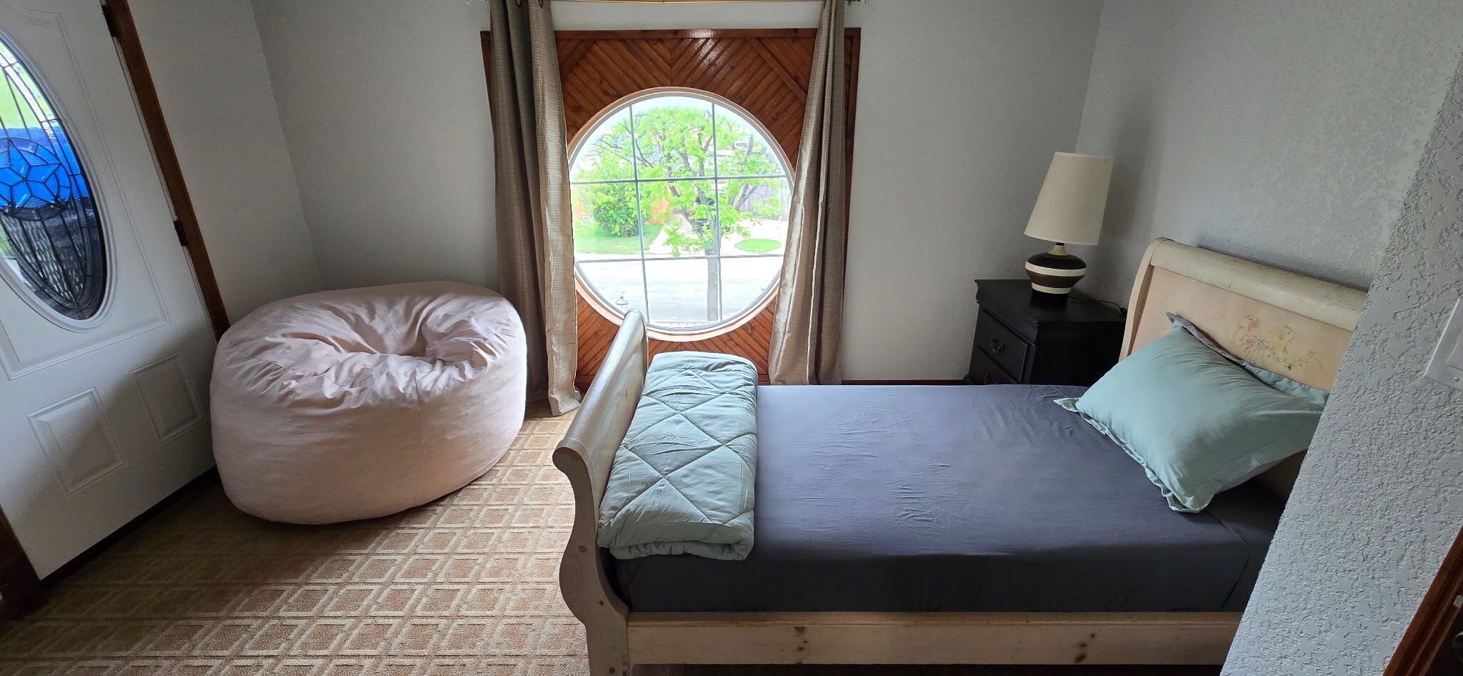 Un dormitorio con cama, un sillón de peluche, una ventana y una mesita de noche.
