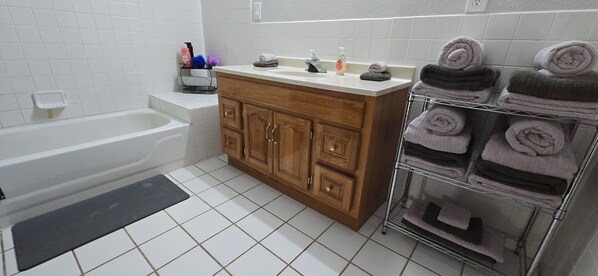 Un baño con tocador de madera, lavamanos, bañera y un perchero para toallas.