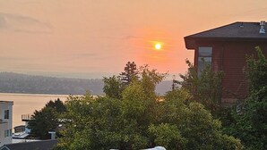 Une terrasse avec un canapé et des coussins, offrant une vue sur un coucher de soleil et une étendue d’eau.