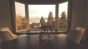 Une baie vitrée offrant une vue sur une étendue d’eau, des arbres et un bâtiment situé de l’autre côté.