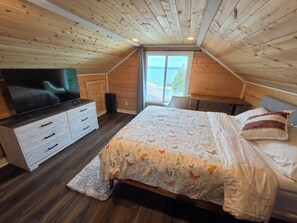 Un dormitorio con techo de madera, una cama con ropa de cama floral, un televisor en una cómoda y una ventana con vistas.