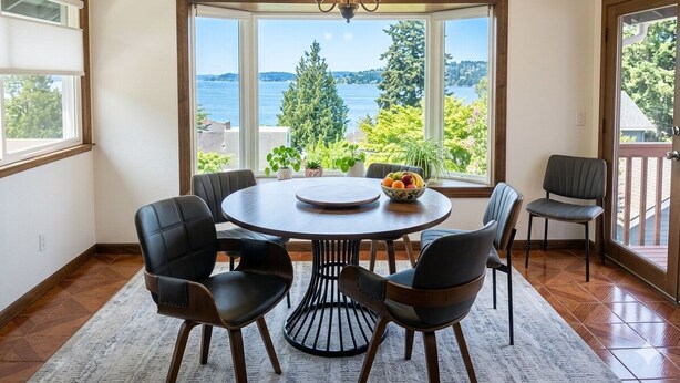 Un coin repas comprenant une table ronde, six chaises, un lustre et une vue sur un lac.