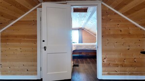 Un intérieur en bois avec une porte blanche donnant sur une chambre dotée d’un plafond en pente et d’une fenêtre.
