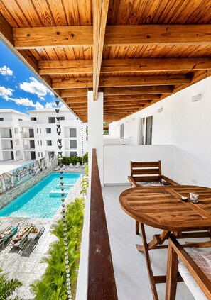 Una terraza de madera con piscina, una mesa con sillas y vistas a un complejo de edificios blancos.