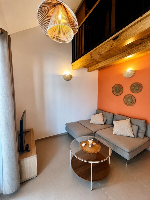 Una sala moderna con un sofá gris, una mesa de centro redonda y una lámpara colgante.