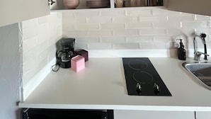 Una cocina con gabinetes blancos, encimera negra, cafetera, tostadora y lavavajillas.